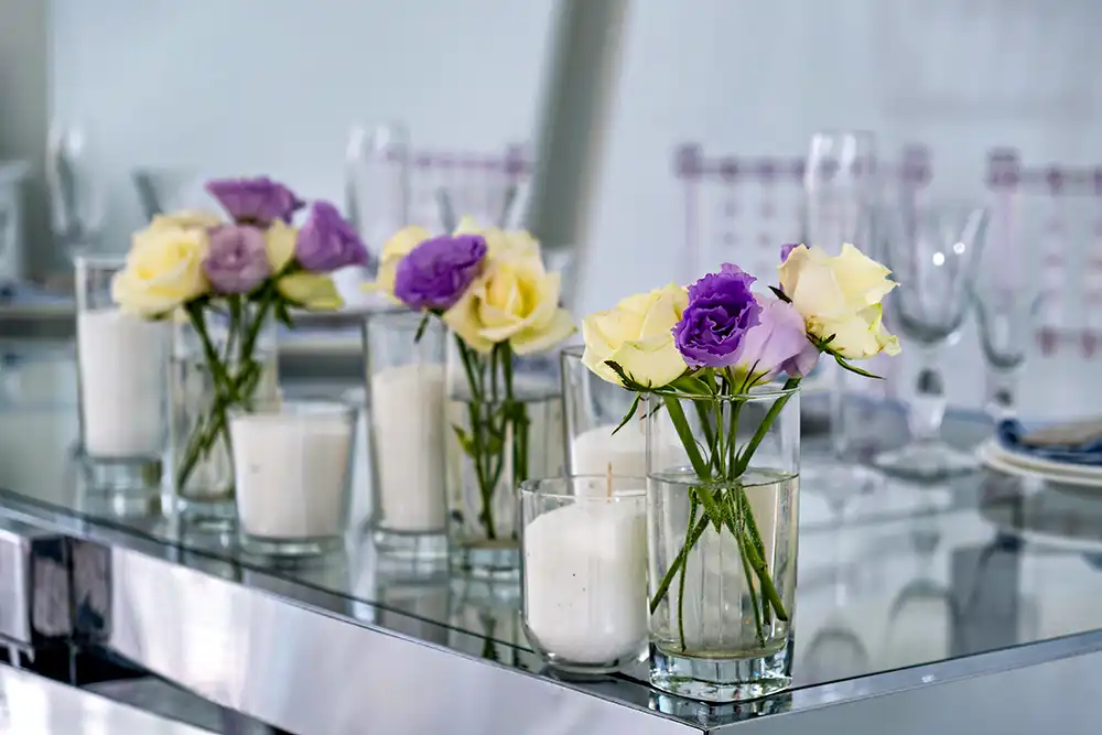 Eine Glasvase mit einem Strauß aus violetten und gelben Rosen und weißen Kerzen