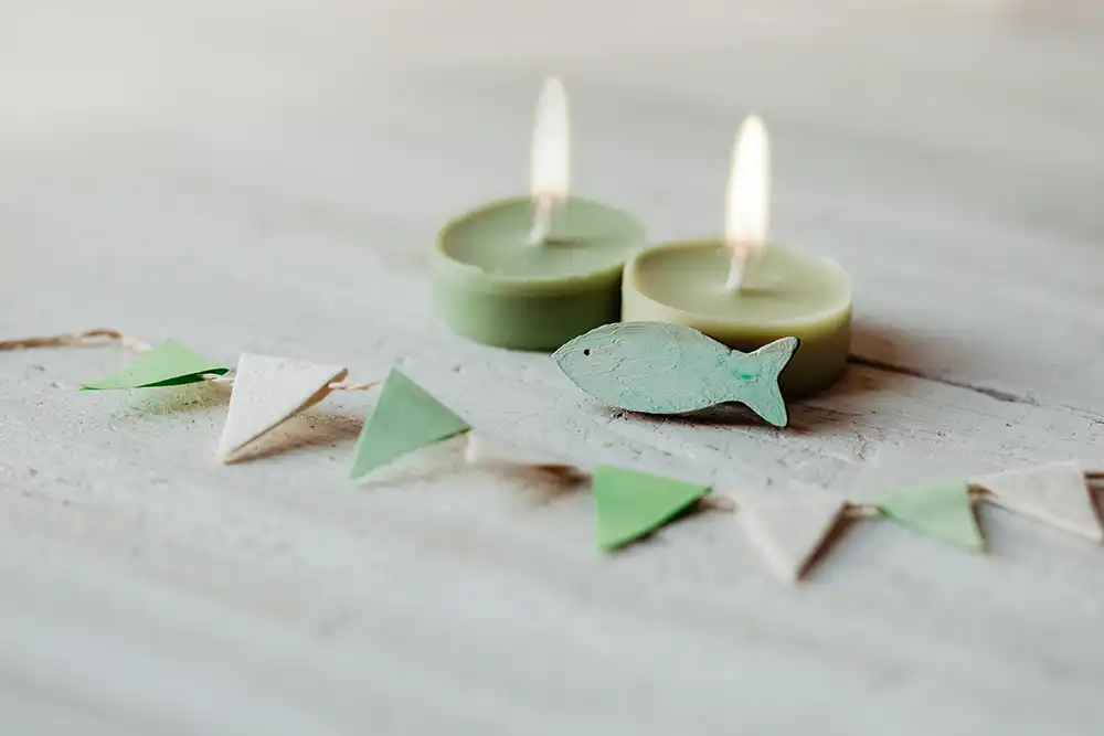 Kommunion, Konfirmation, Firmung, Taufe - Fisch aus Holz auf weißem Holz vor grünen Teelichtern mit Wimpel Girlande