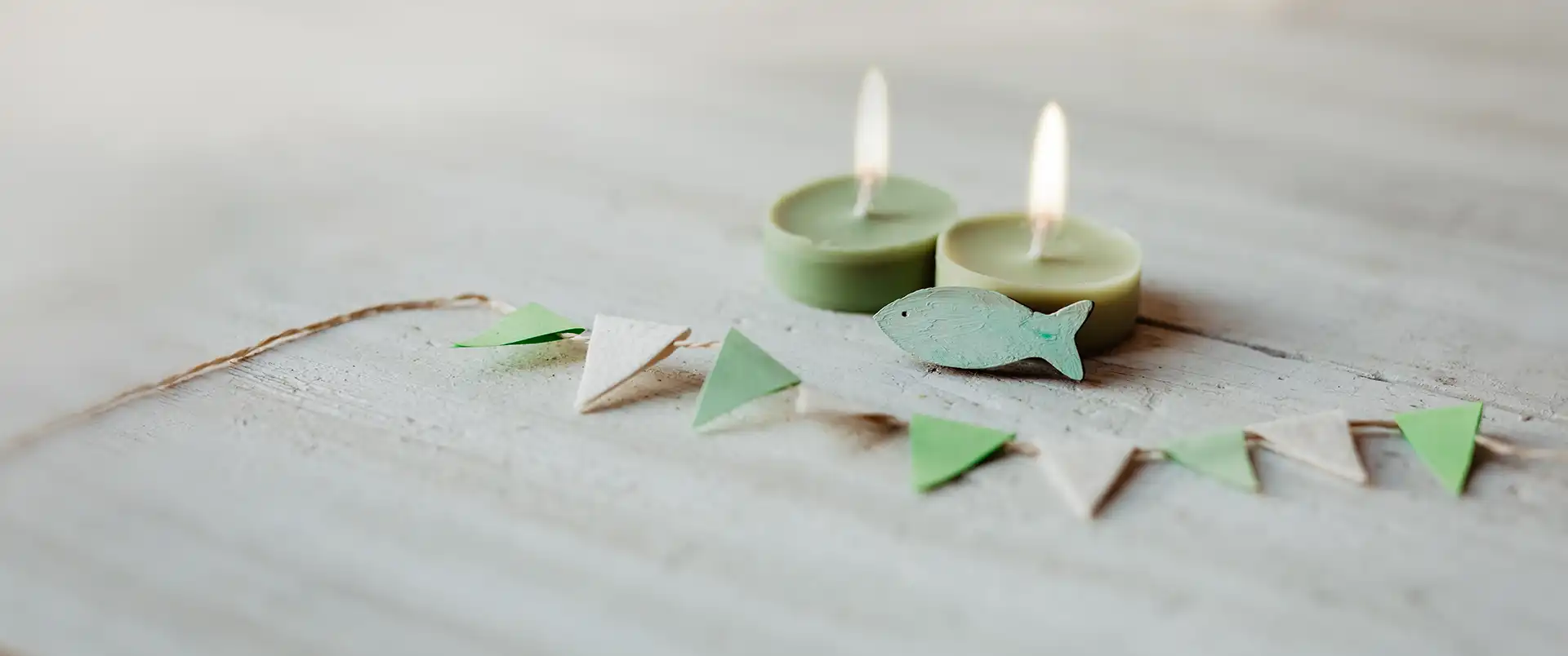Kommunion, Konfirmation, Firmung, Taufe - Fisch aus Holz auf weißem Holz vor grünen Teelichtern mit Wimpel Girlande
